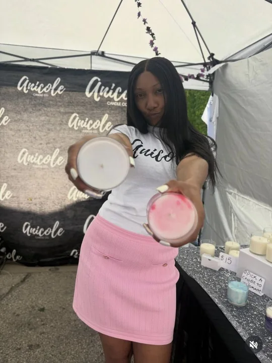 Owner of Anicole Candle Co holding candles at an outdoor booth